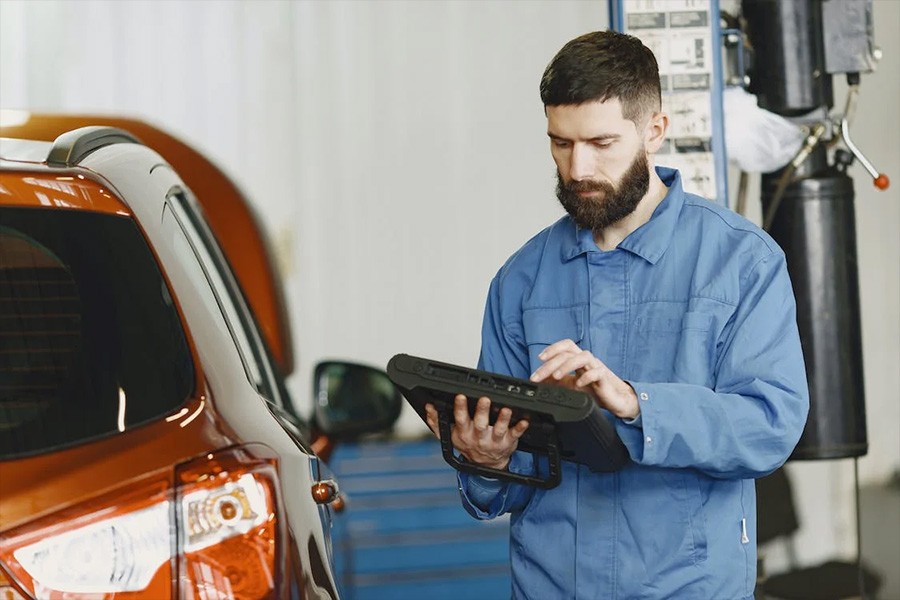 Man in blue coverall using an automotive diagnostic tool