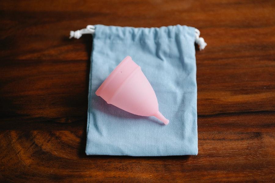 Pink reusable menstruation cup on a blue bag