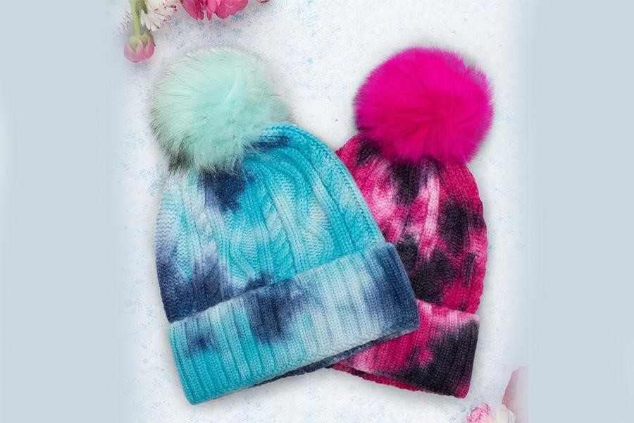 Two tie-dye pompom beanies displayed on a table
