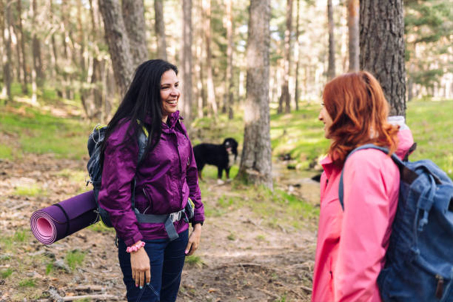 Two women in woods with lightweight jackets and yoga mats