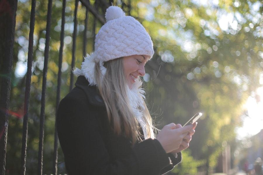 Woman holding her phone while wearing a pom-pom beanie