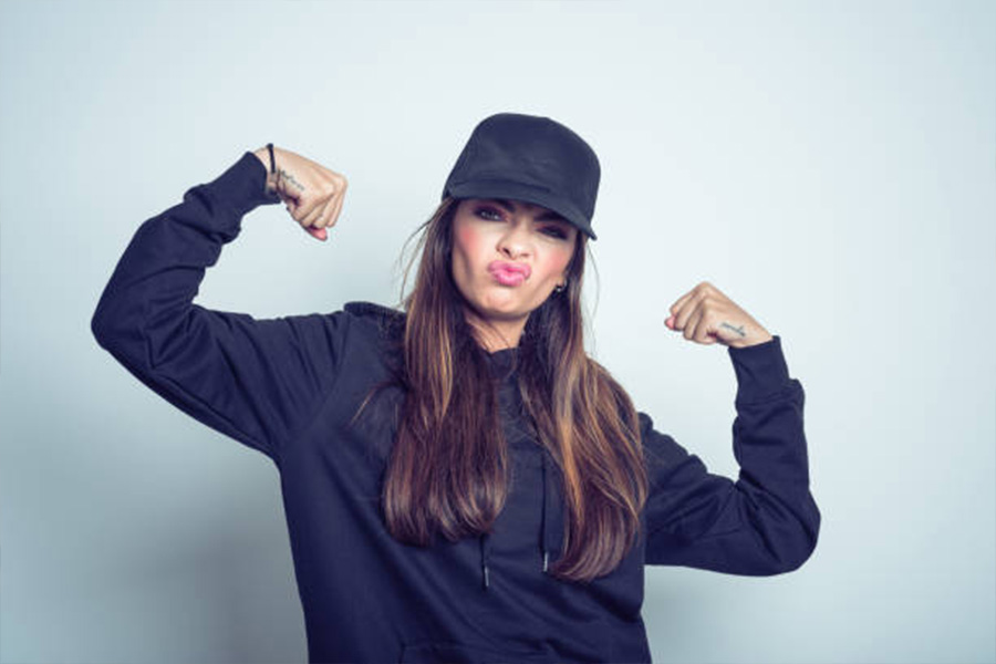 Woman in black hoodie and baseball hat in strong pose
