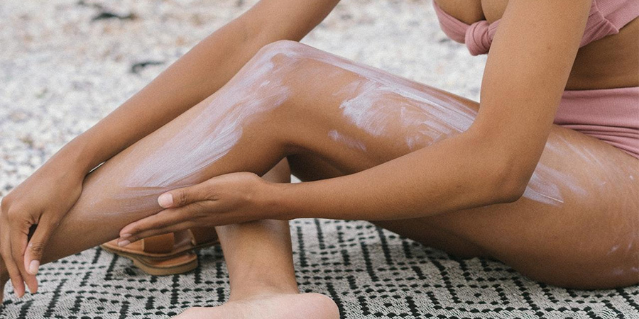 woman on the beach applying sunscreen to her leg