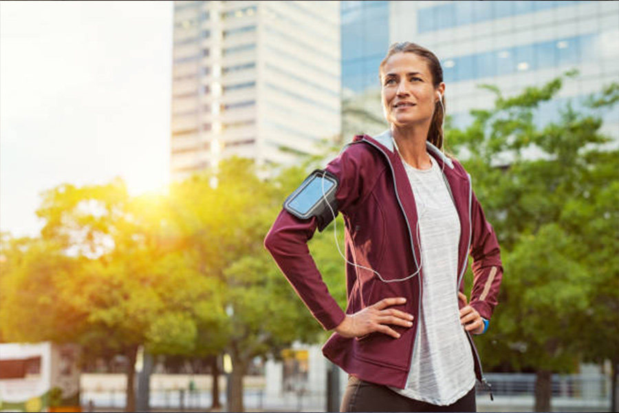 Woman pausing from run wearing activewear jacket and headphones