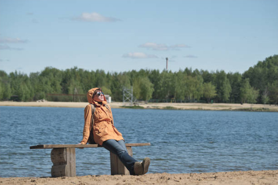 Woman sitting next to lake in active outerwear jacket