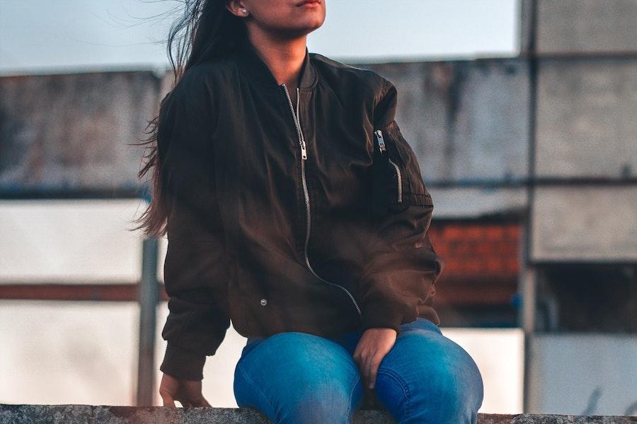 Woman sitting on a fence with a black bomber jacket