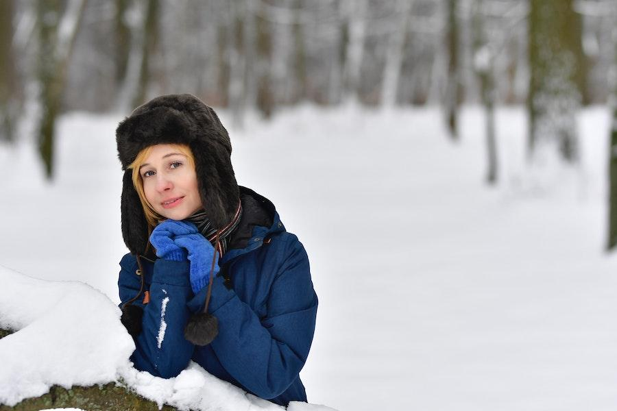 Woman sitting on the snow in a black trapper hat