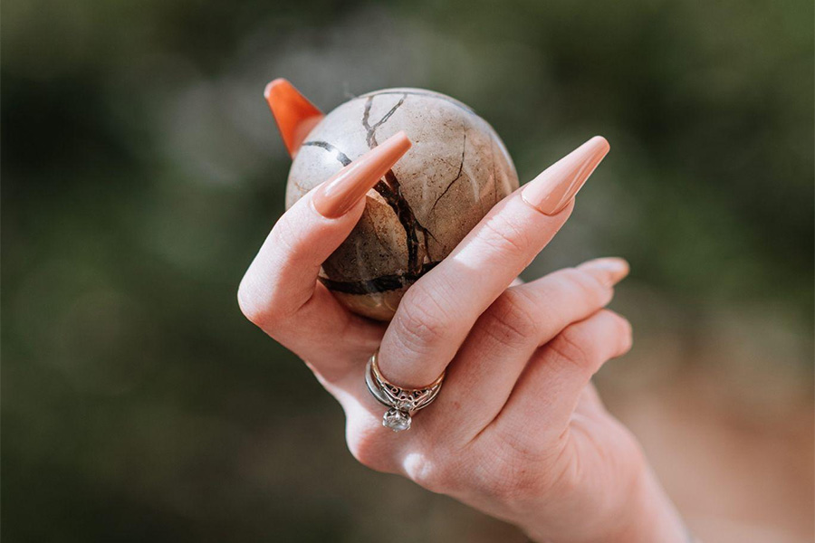 Woman with long, beige acrylic nails holding a ball.