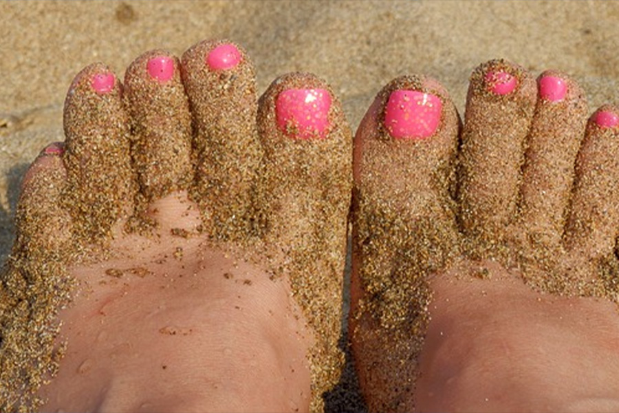 Woman's sandy feet with hot pink polish.