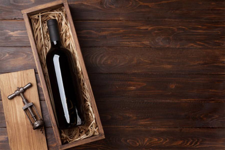 Wooden box holding wine bottle with corkscrew beside it