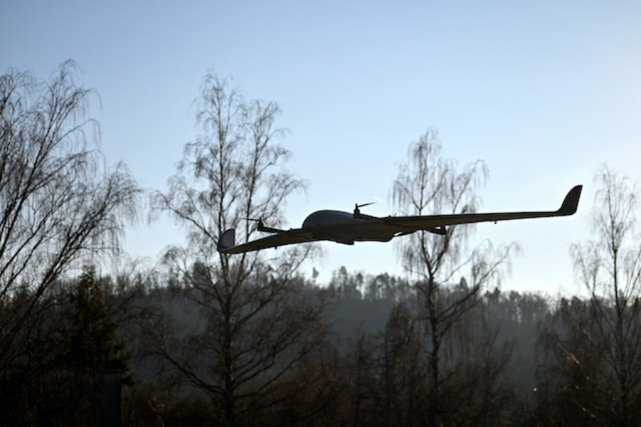 A fixed-wing drone flying in front of four birch trees
