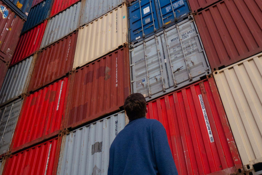 A man in blue jacket standing in front of red and blue containers