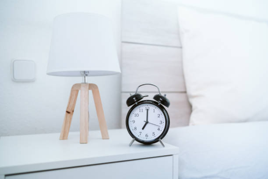 A white nightstand with alarm clock and lamp on top