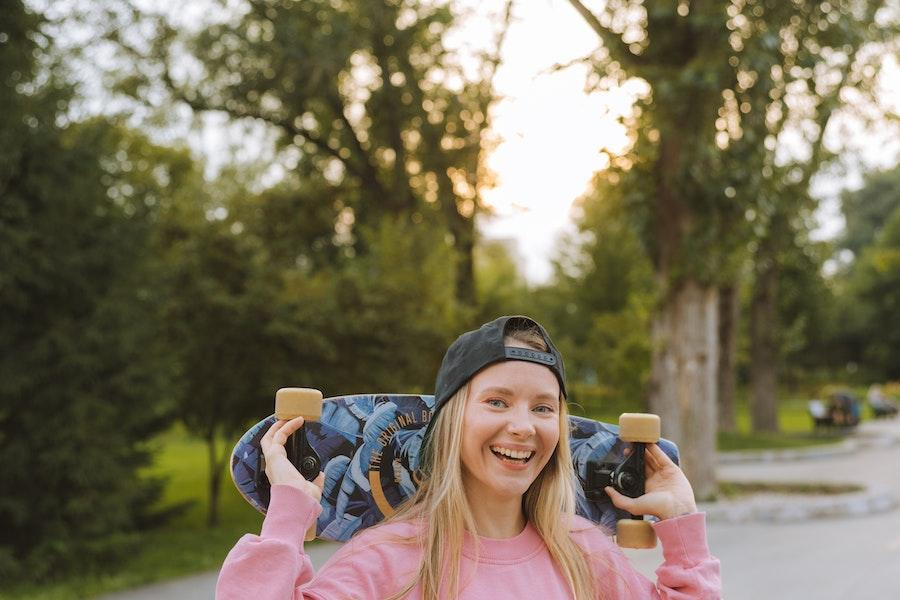 Blonde lady wearing a baseball cap and holding a skateboard