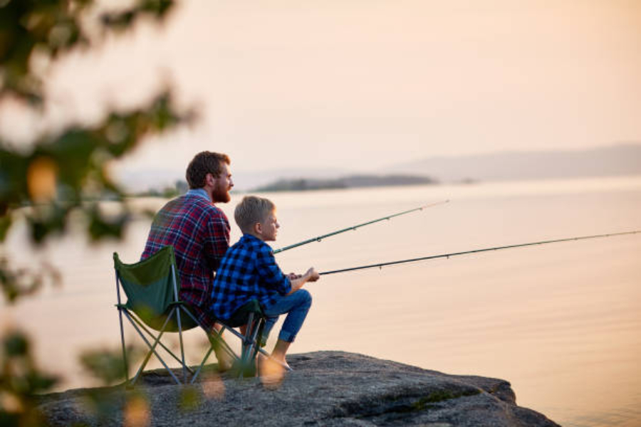 Father and son at sunrise sitting on rock fishing