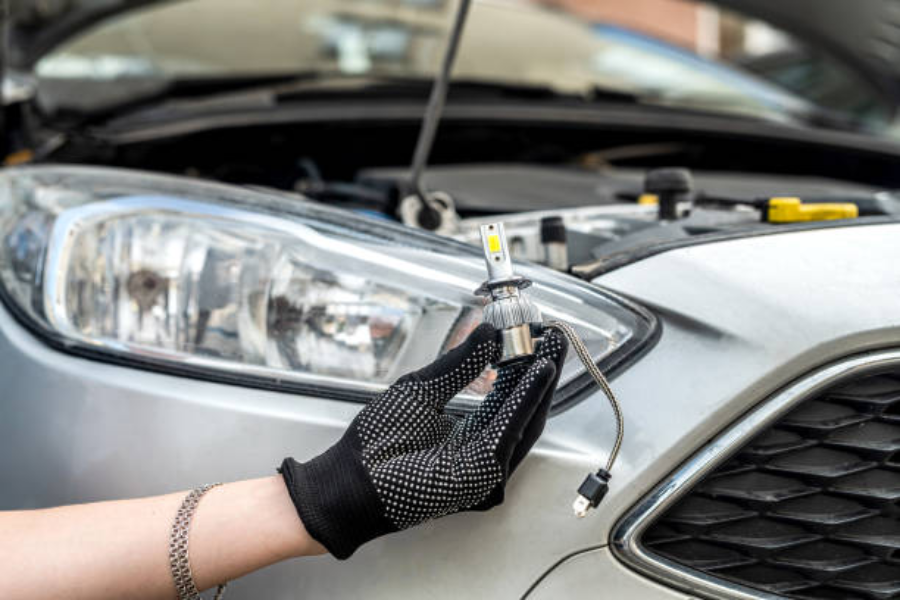 A hand holding modern LED bulb near a car headlamp
