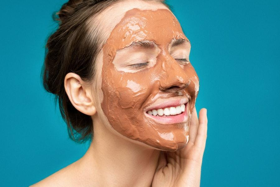 Lady applying a brown face mask on her face