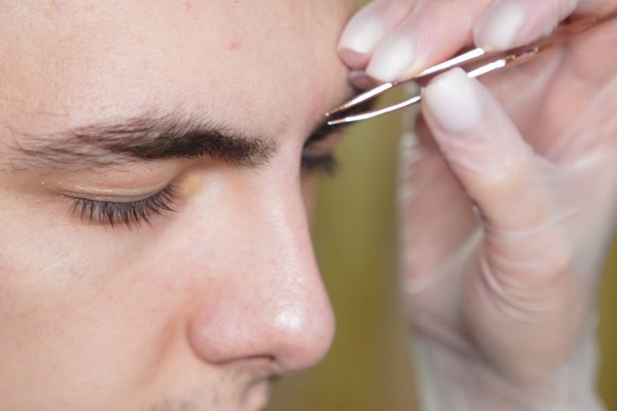 Man getting his eyebrow trimmed with tweezers