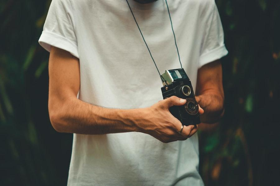 Man holding a camera while wearing a white boxy tee