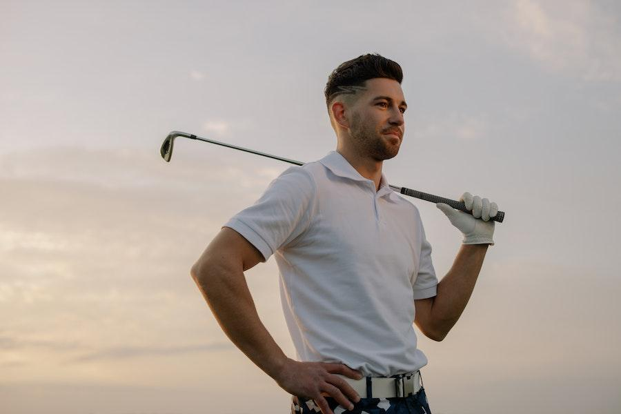 Man posing with golf club while rocking white polo
