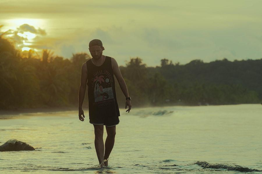 Man walking on a beach while wearing graphic tank top