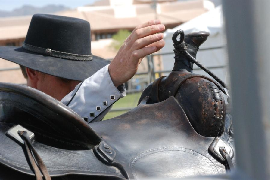 man wearing a black cowboy hat while saddling up