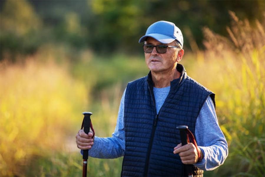Man with hiking poles wearing a baseball cap and sunglasses