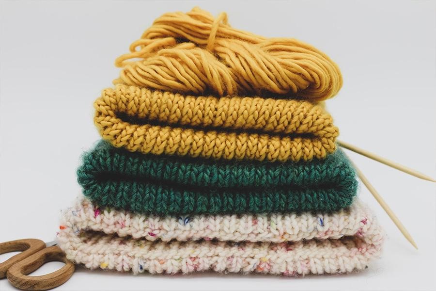 Stack of knitted hats with yarn, needles, and scissors