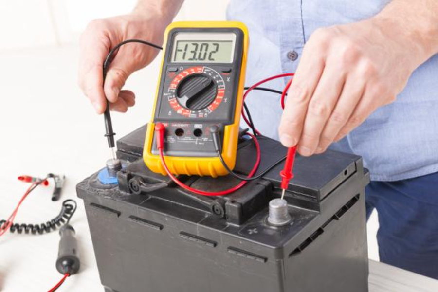 Technician taking the voltage reading of car battery with multimeter