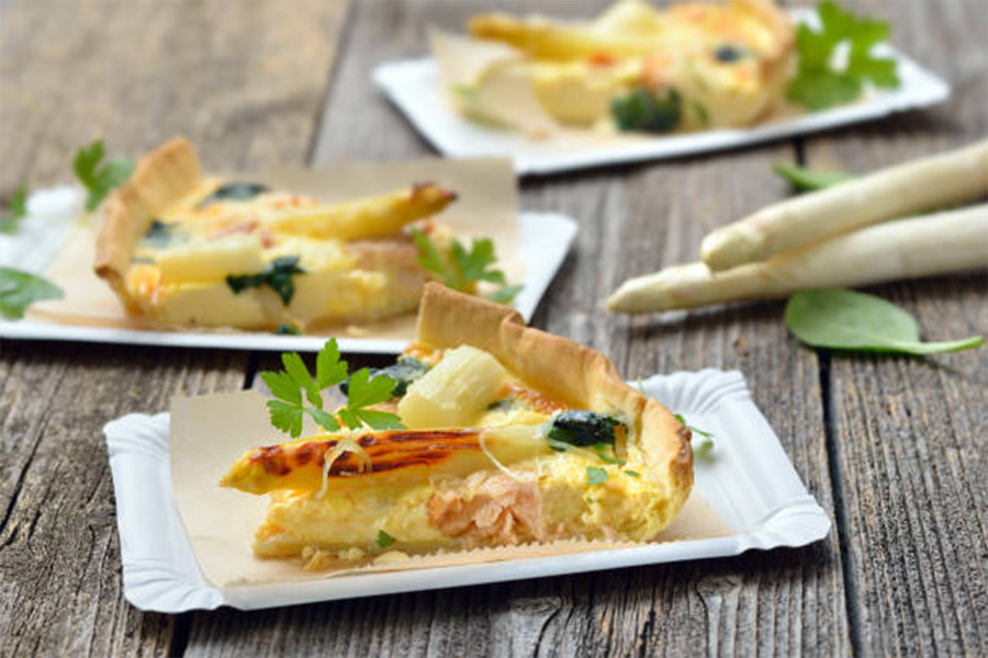White paper plates with fresh quiche slices on top