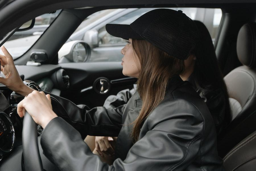 Woman driving in a leather jacket and black baseball cap