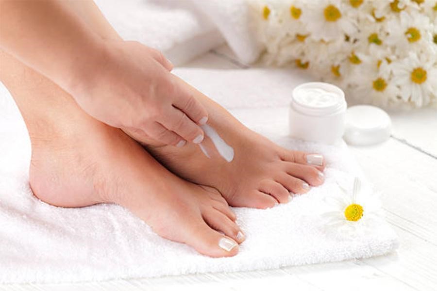 Woman putting lotion on foot on top of bathroom towel