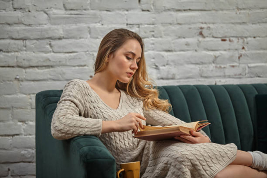 Woman sitting on a couch reading in long sleeve dress