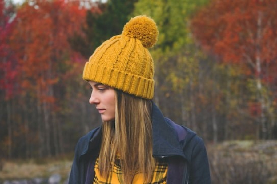 A woman wearing a yellow cable knit pom-pom beanie hat