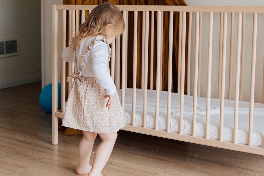 Little girl standing beside a baby crib