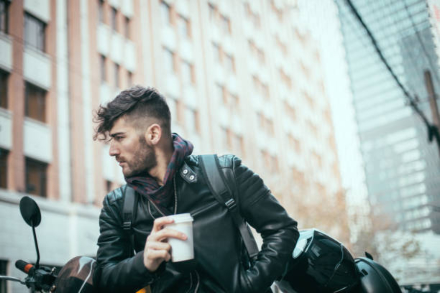 Man in city wearing black leather jacket holding coffee cup